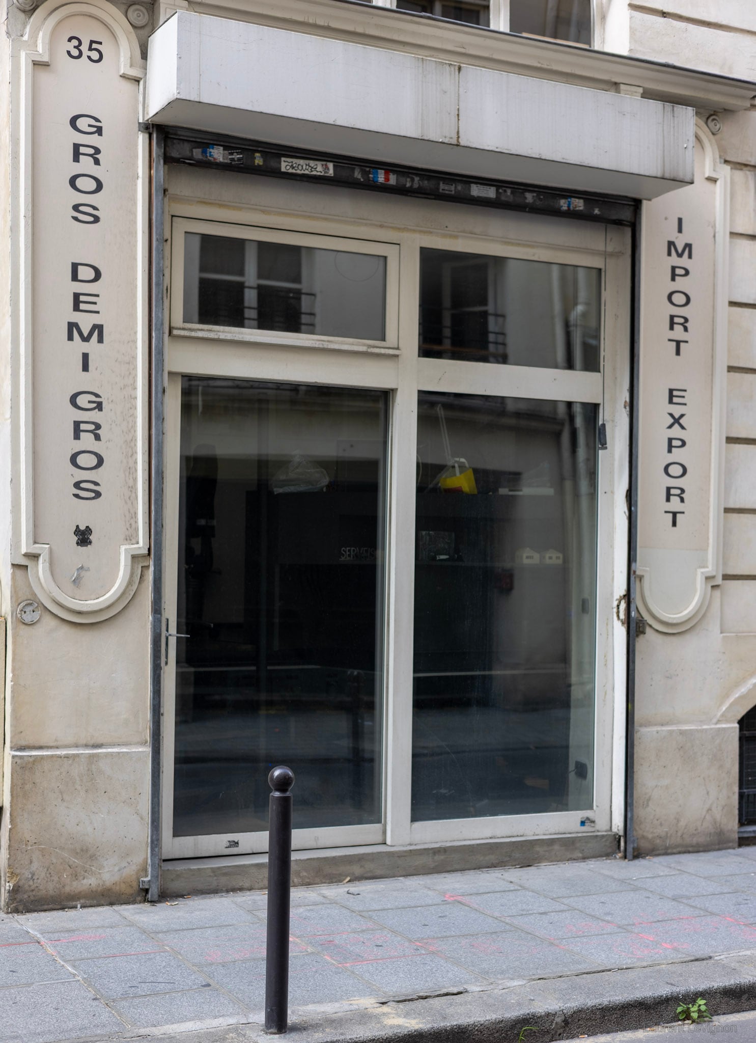 Une vitrine vide, ses deux inscriptions et une borne. Le Sentier, Paris, septembre 2023 — le quartier du textile en gros, dont les boutiques ferment une à une.